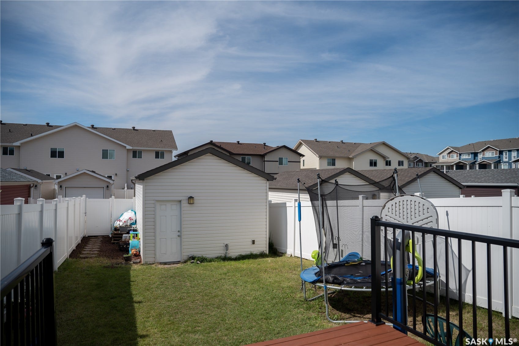 Backyard featuring a detached shed, white privacy fencing, a wood deck, and a manicured lawn