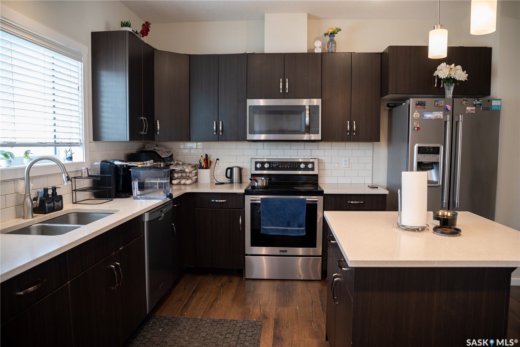 Kitchen featuring dark wood-finish cabinetry, light-toned countertops, stainless steel appliances, a subway tile backsplash, and wood-finish flooring