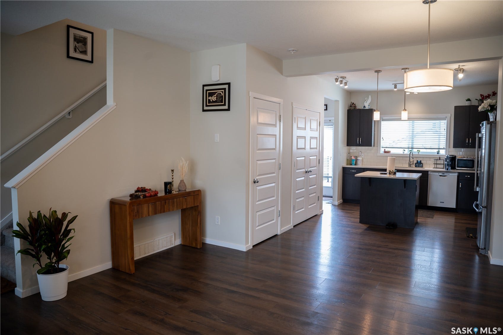 Wood-finish flooring throughout, bright neutral wall paint, white trim, dark cabinetry, and a central kitchen island