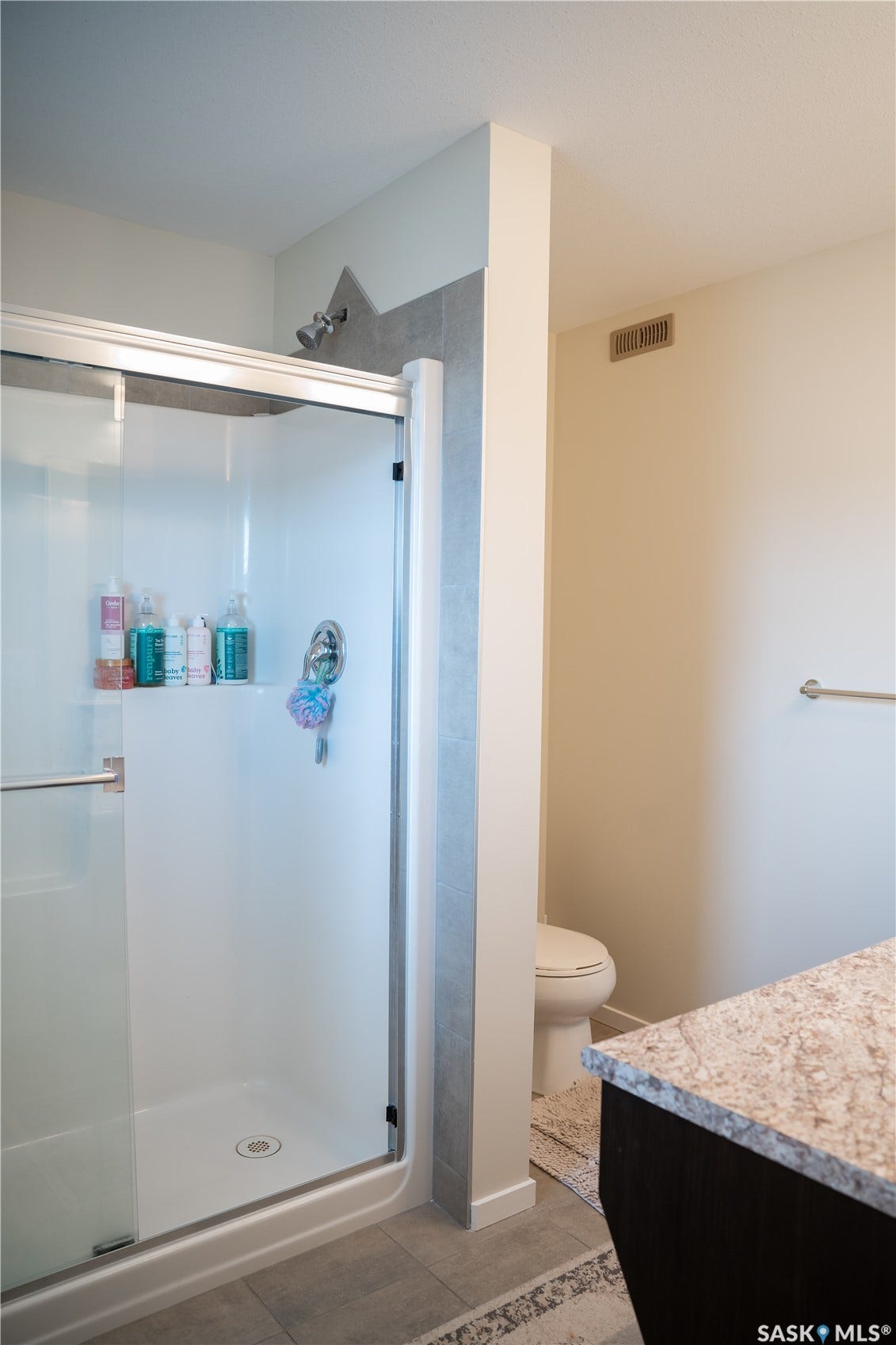Glass-enclosed shower with a gray tiled wall, chrome fixtures, and a white base
