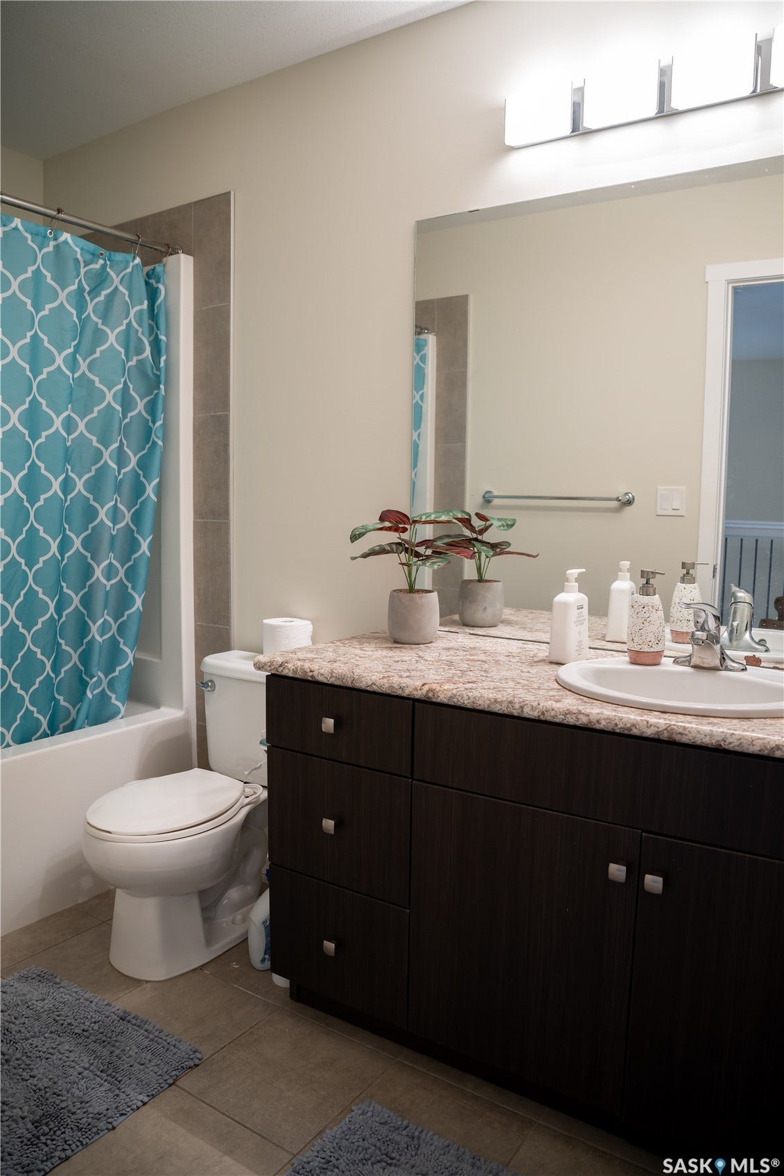 Bathroom featuring a dark wood-finish vanity with a light-colored countertop, an integrated sink, a rectangular wall-mounted mirror, and a tub with tiled surround