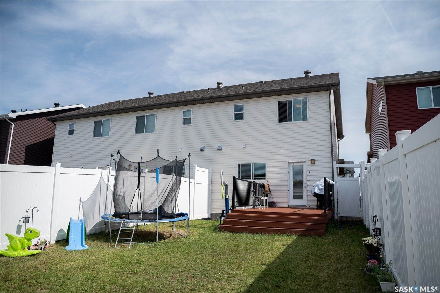 White vinyl siding exterior with a brown shingled roof, featuring a rear wood deck and a grass lawn
