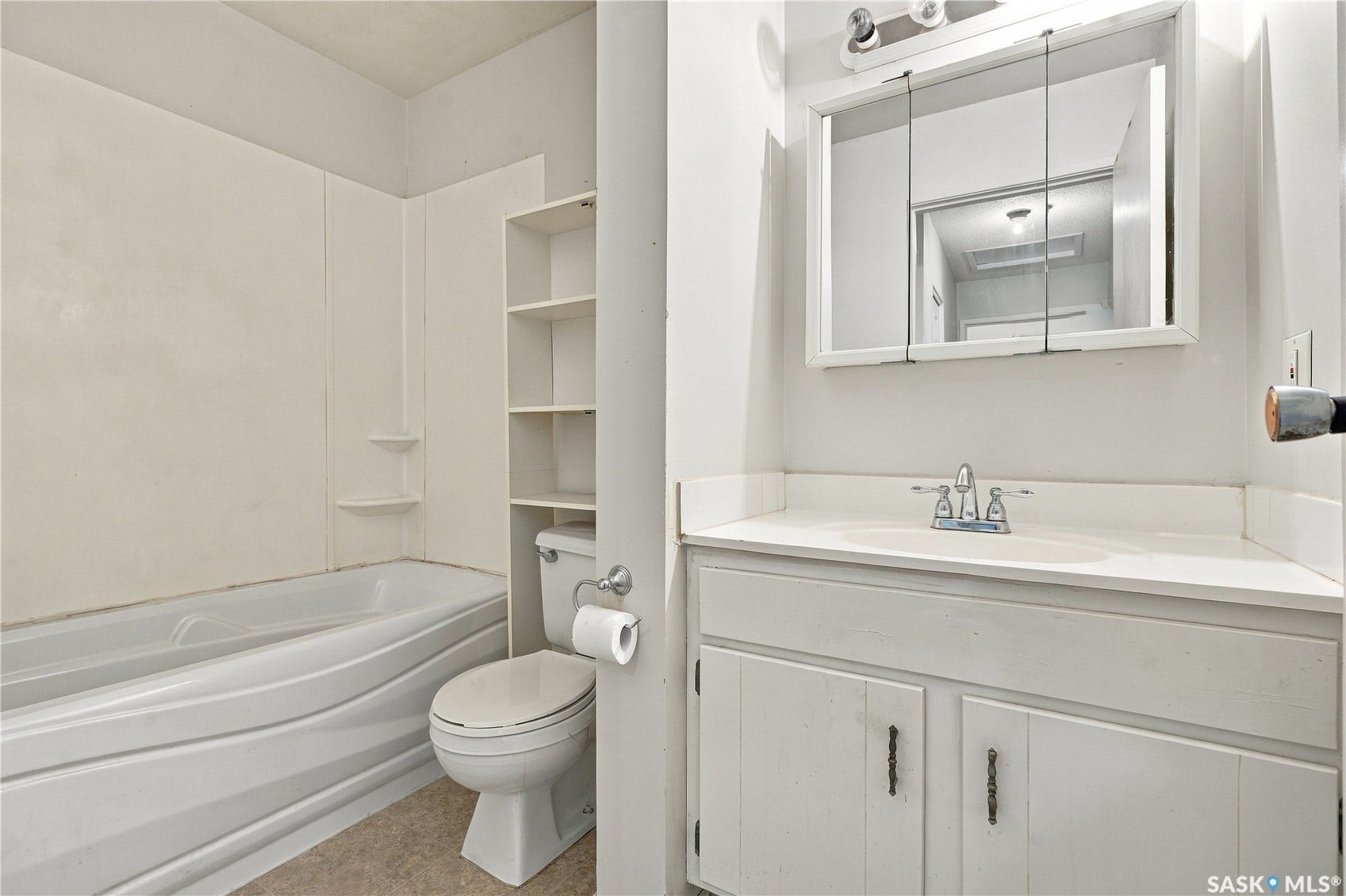 White vanity with a laminate countertop, a medicine cabinet, a toilet, and a built-in tub with a shower surround