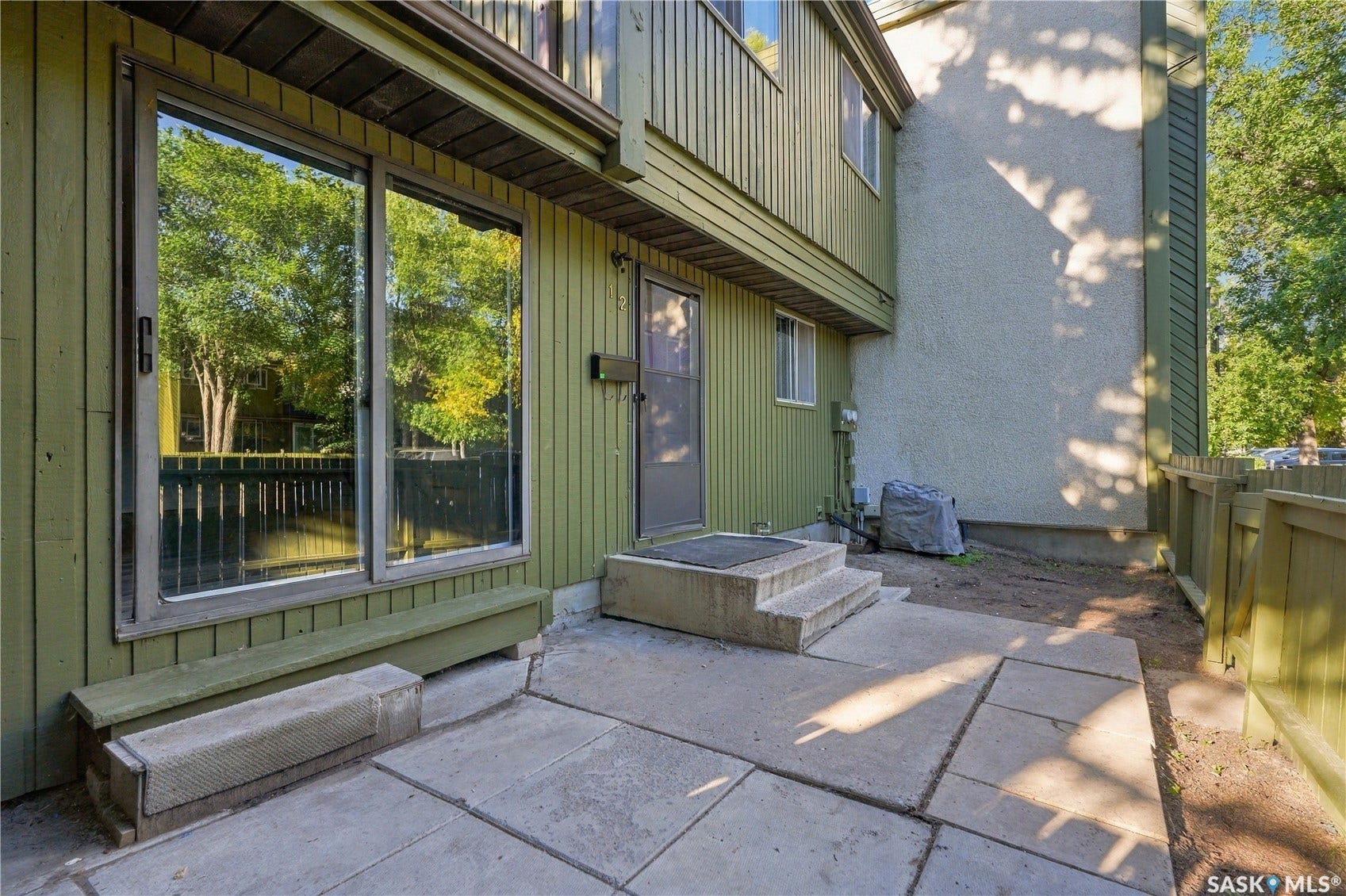 Concrete patio with two-step entry, vertical siding, privacy fencing, and a large sliding glass door