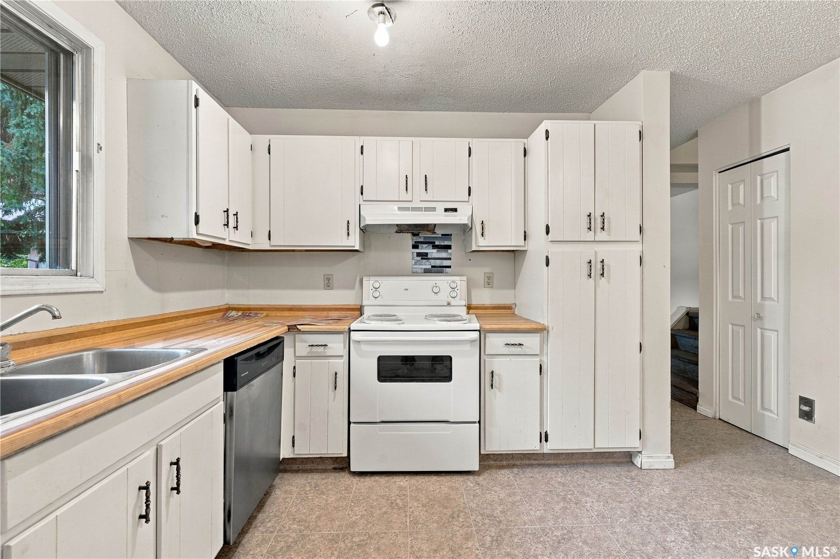 Kitchen featuring white cabinetry, wood-finish countertops, stainless steel dishwasher, double basin sink, and a multi-tone tile backsplash
