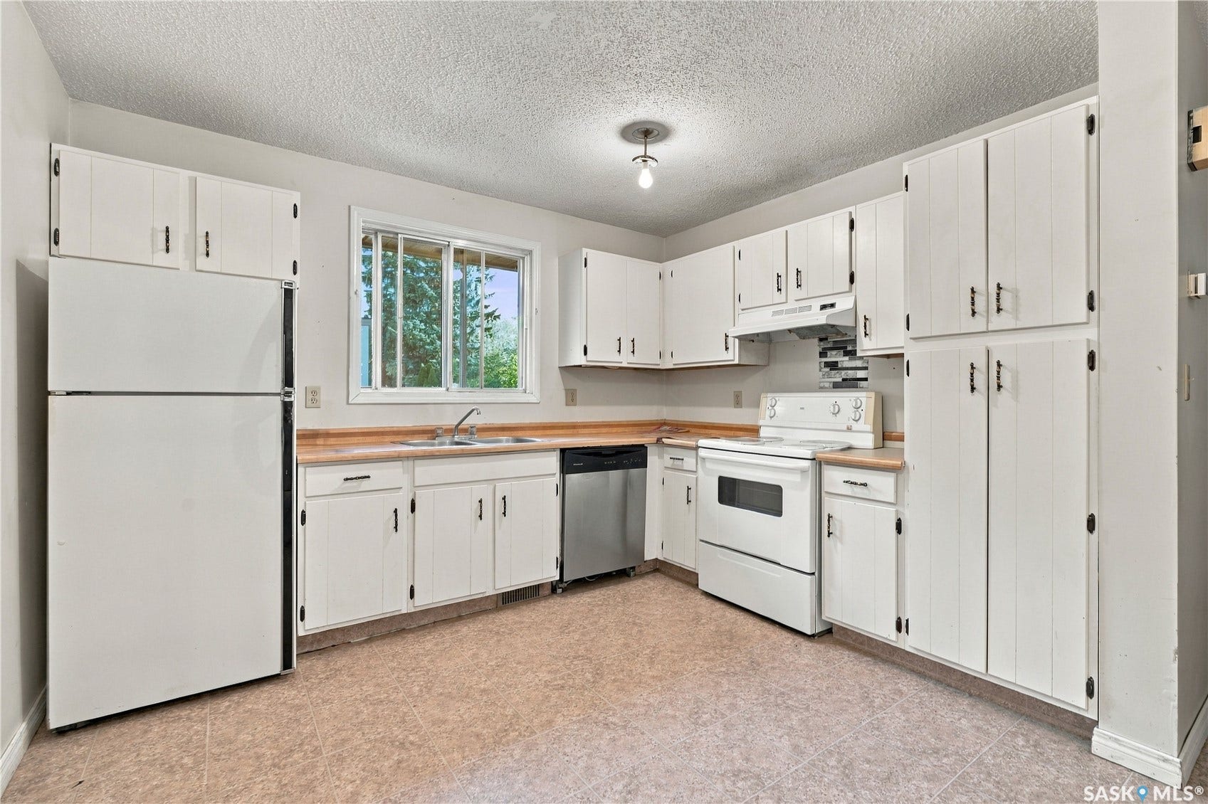 Functional kitchen featuring white cabinetry, a double basin sink, a built-in dishwasher, and a window for natural light
