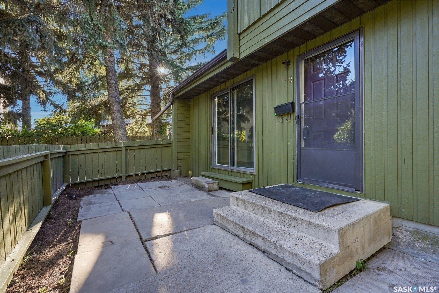 Green exterior siding, concrete patio, wood fence, mature trees, concrete steps