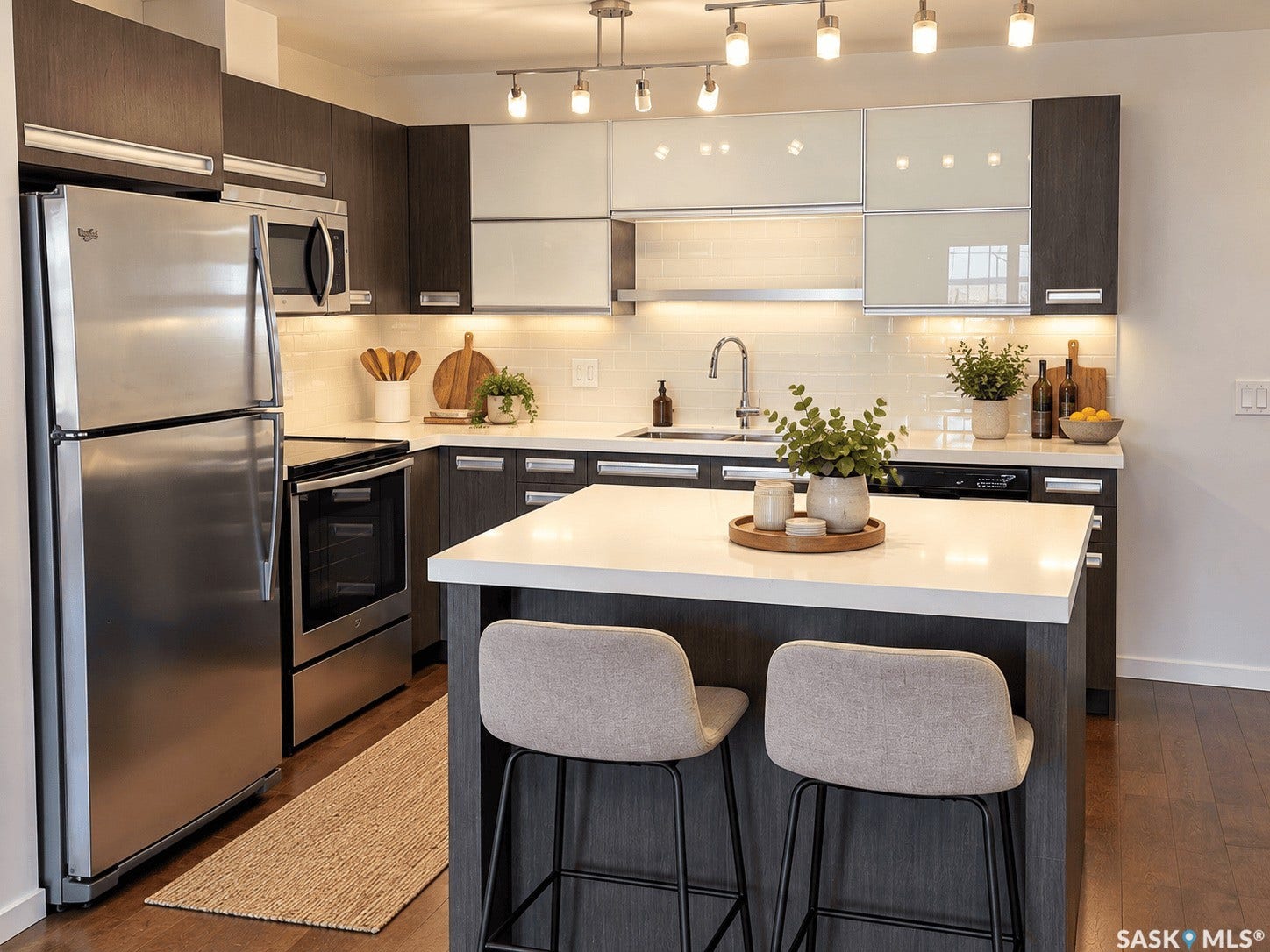 Contemporary kitchen featuring wood-finish flooring, stainless steel appliances, a center island with countertop seating, white subway tile backsplash, and dark wood-finish cabinetry with white upper cabinets