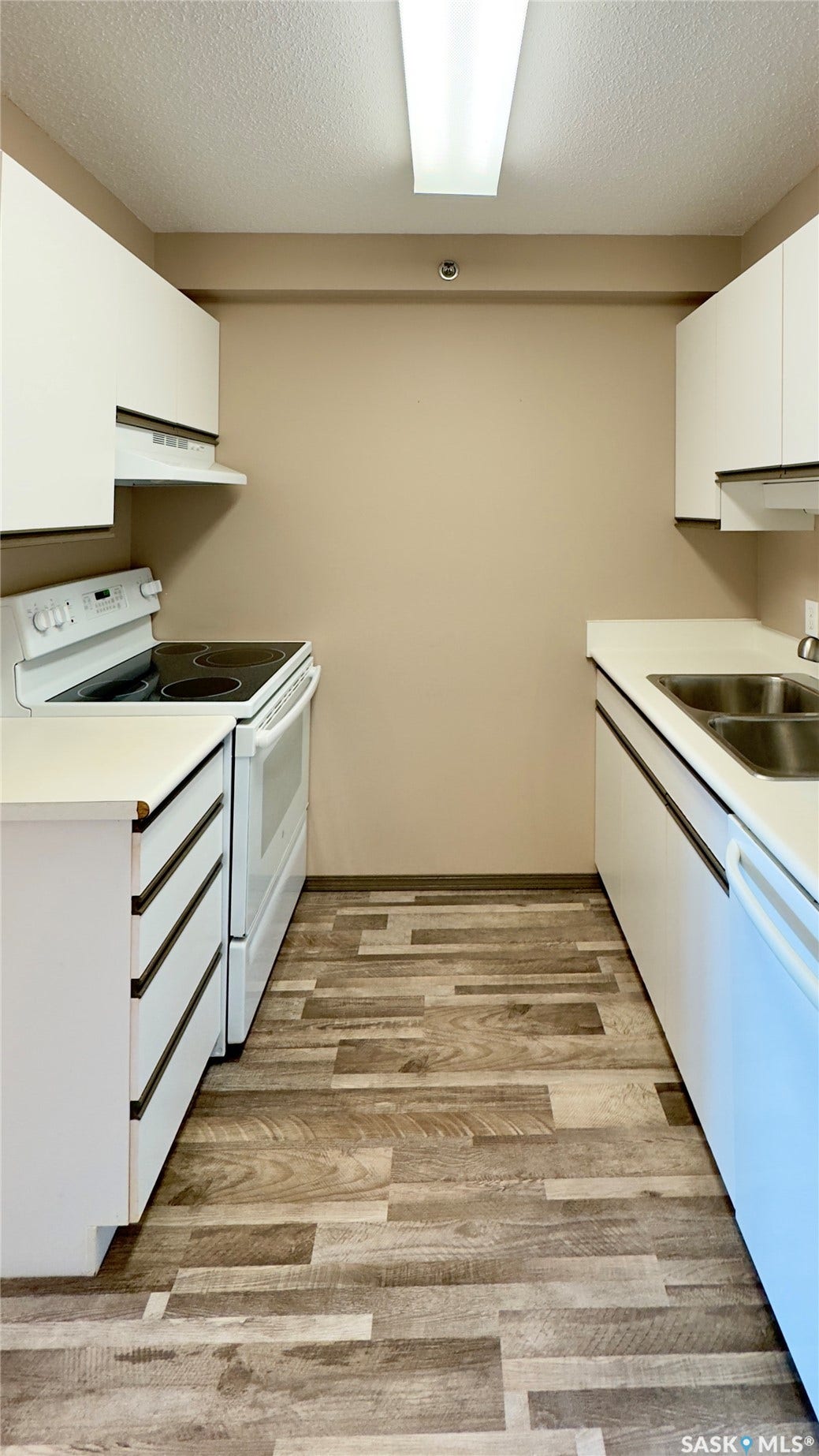 Galley-style kitchen with white cabinetry, wood-finish flooring, white appliances, and a double basin sink