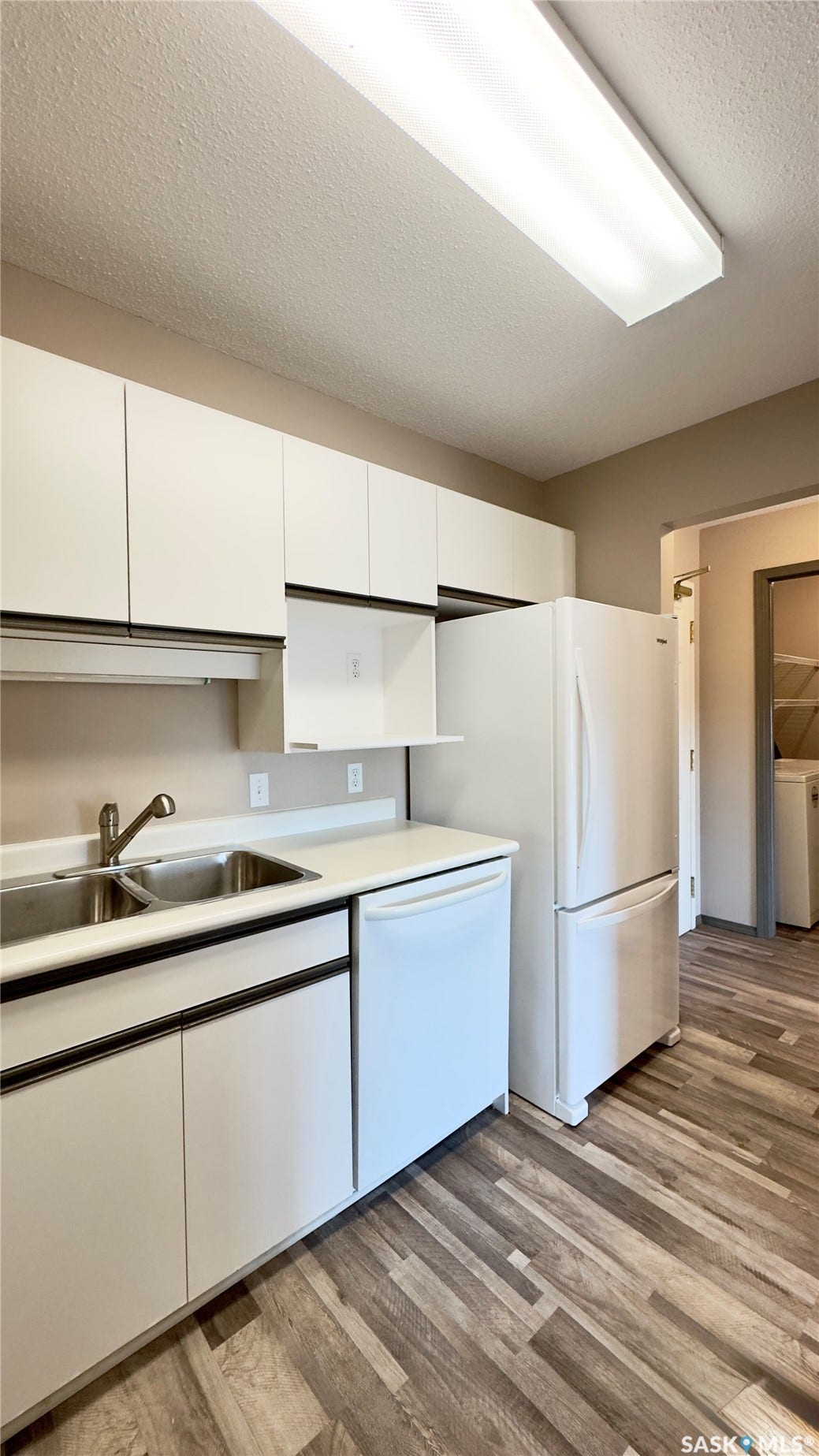White cabinetry, wood-finish flooring, dual basin sink, white appliances, and overhead fluorescent lighting