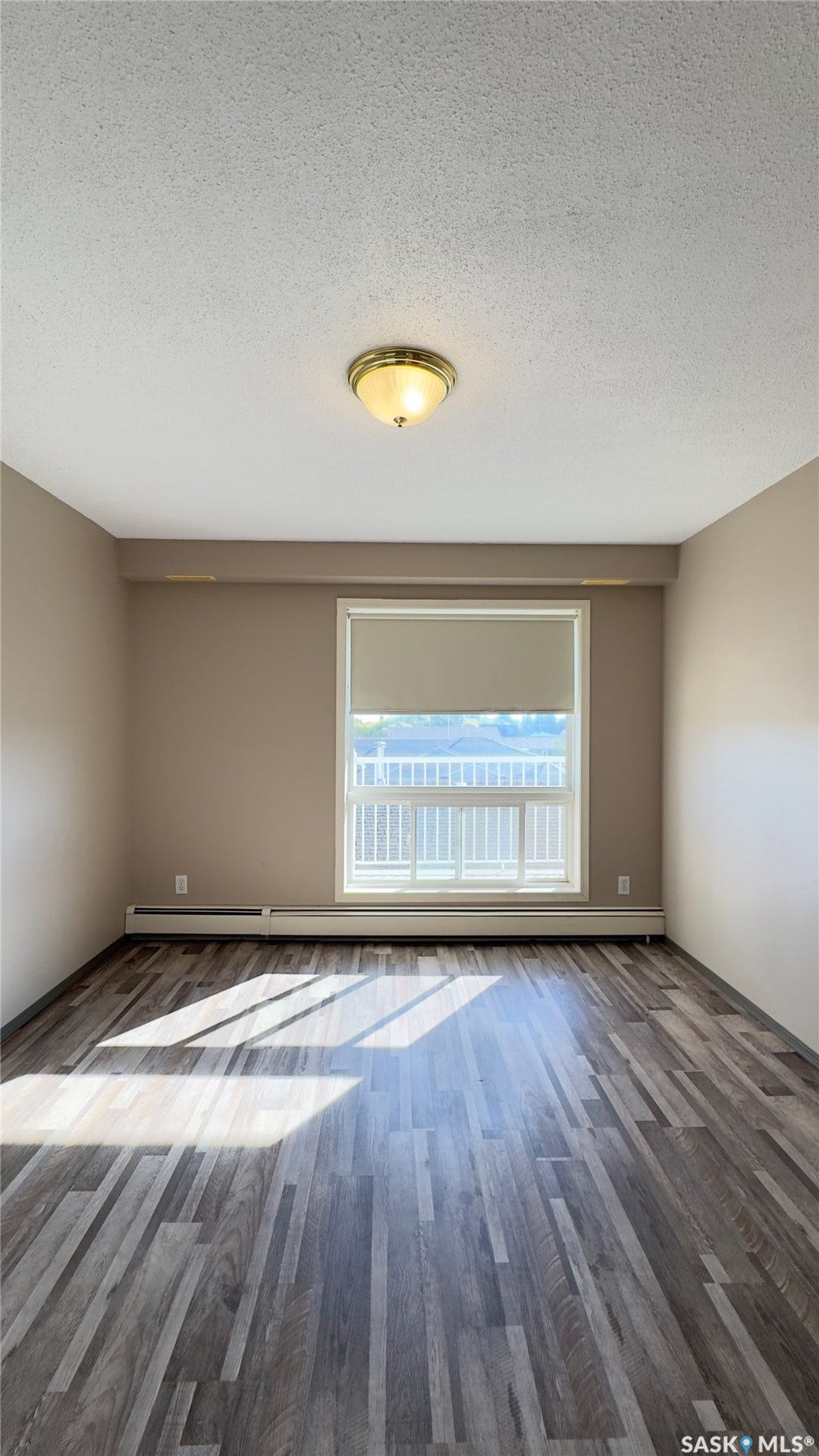 Wood-finish flooring with a large window, roller shade, and ceiling-mounted light fixture