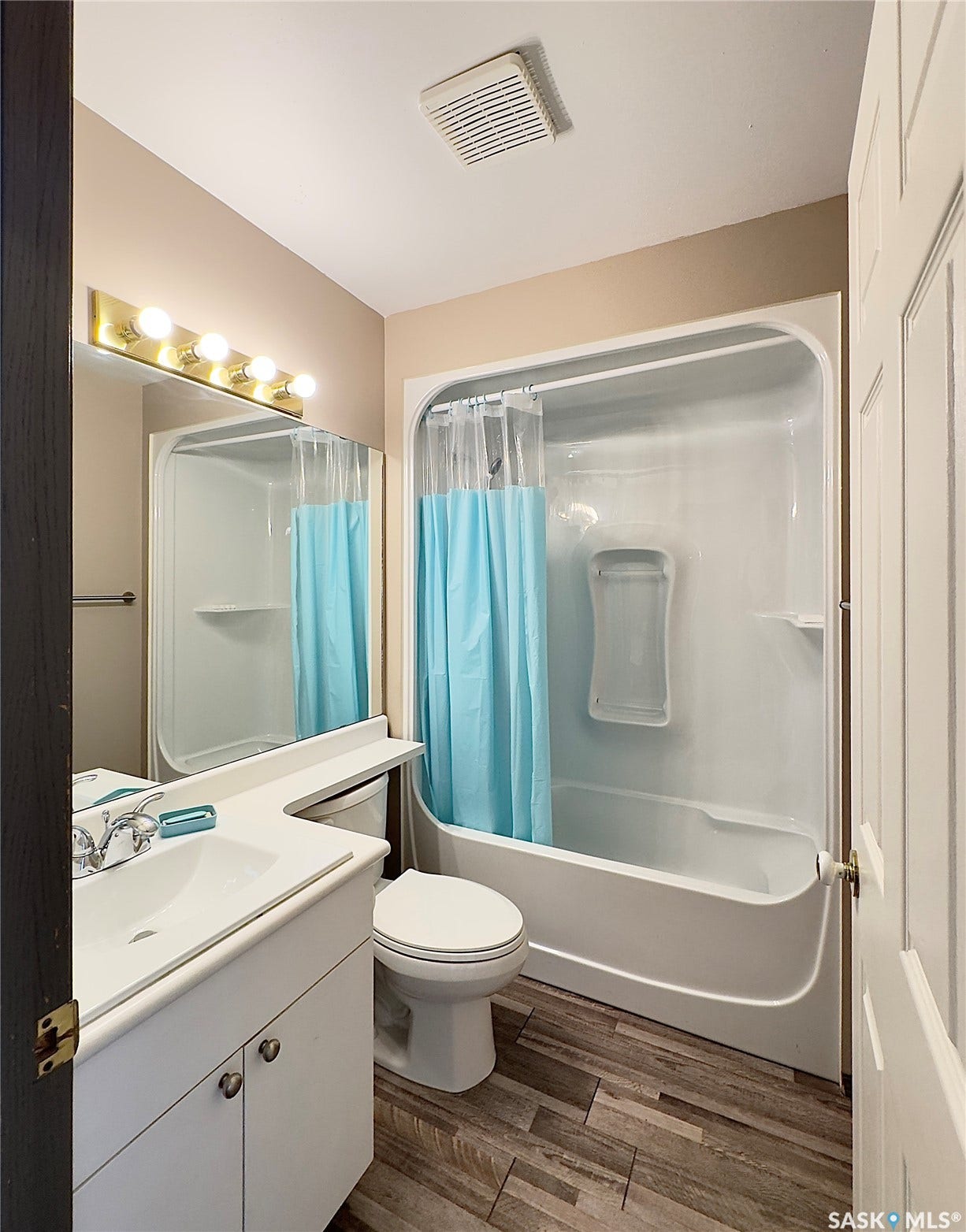 White vanity with integrated sink, wood-finish flooring, and a shower-over-tub combination with white surround