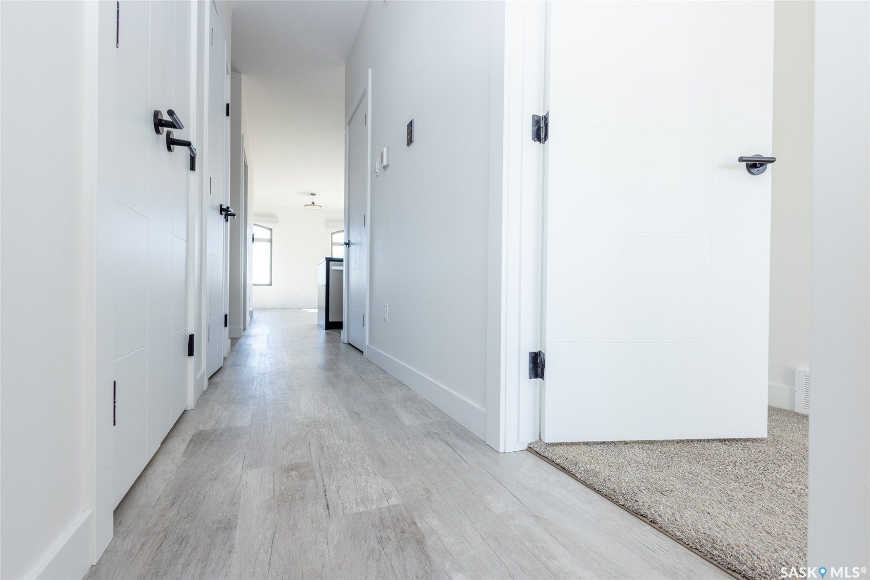 Hallway featuring wood-finish flooring, white panel doors, and matte black hardware