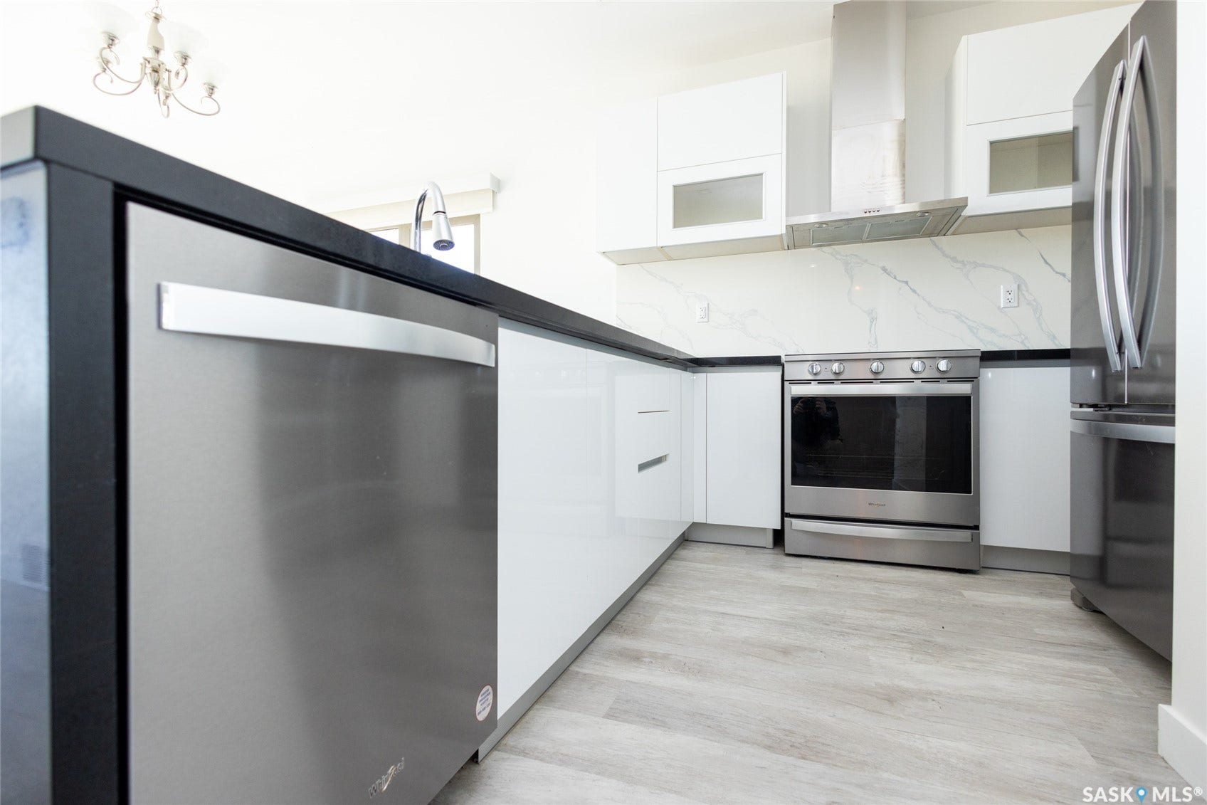 Modern kitchen featuring stainless steel appliances, light wood-finish flooring, white cabinetry, and a stone-finish backsplash