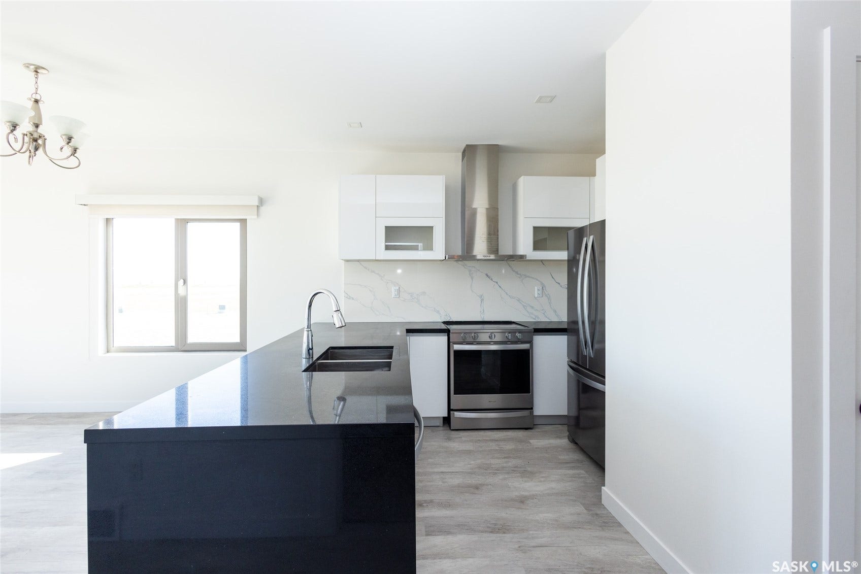 Kitchen featuring a large island with an integrated sink, stainless steel appliances, white flat-panel cabinetry, and a full-height backsplash