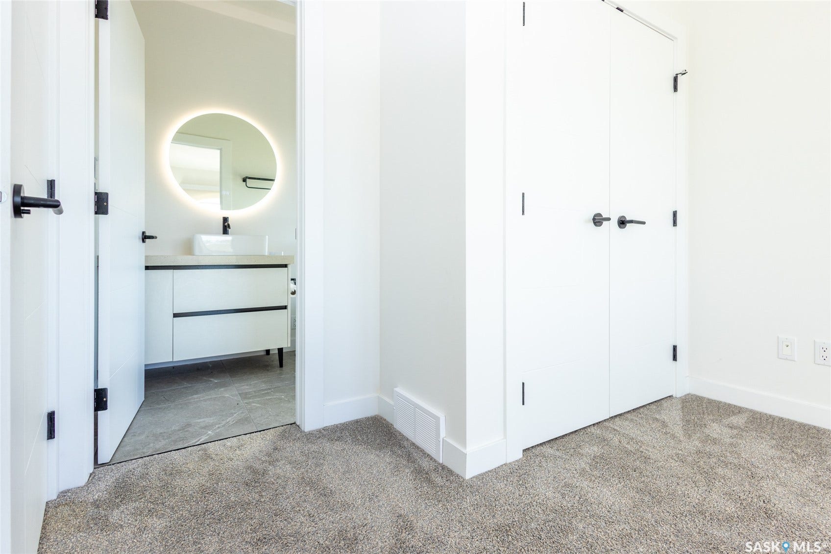 Modern vanity with vessel sink, illuminated circular mirror, and sleek matte black hardware
