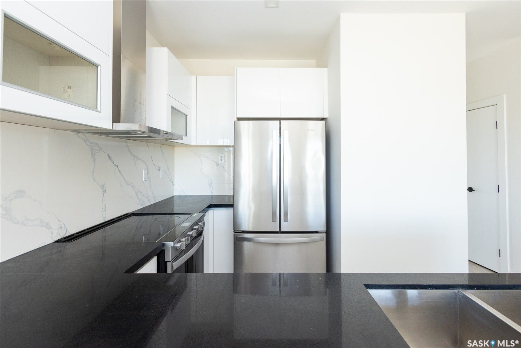 U-shaped kitchen featuring black countertops, white cabinetry, integrated stainless steel range, stainless steel refrigerator, and white backsplash