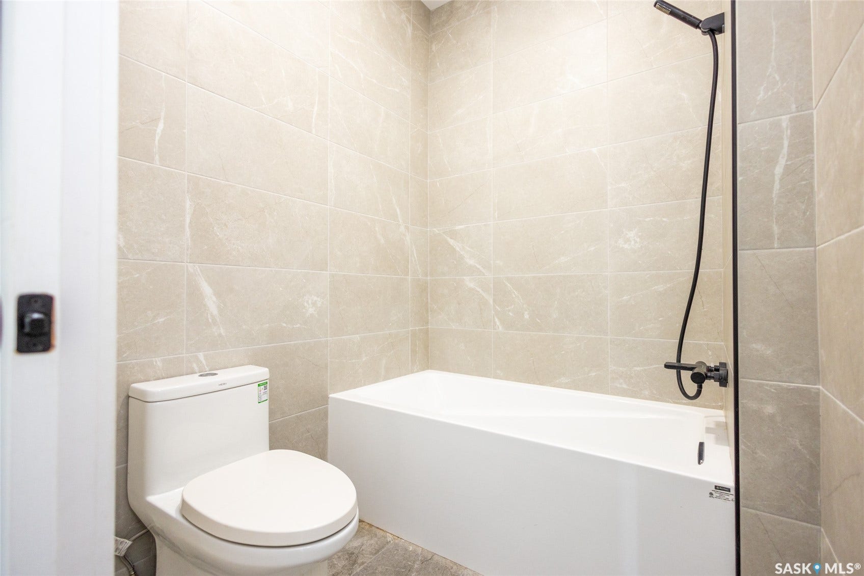 Integrated bathtub and shower with matte black fixtures, full-height wall tiling, and a white toilet