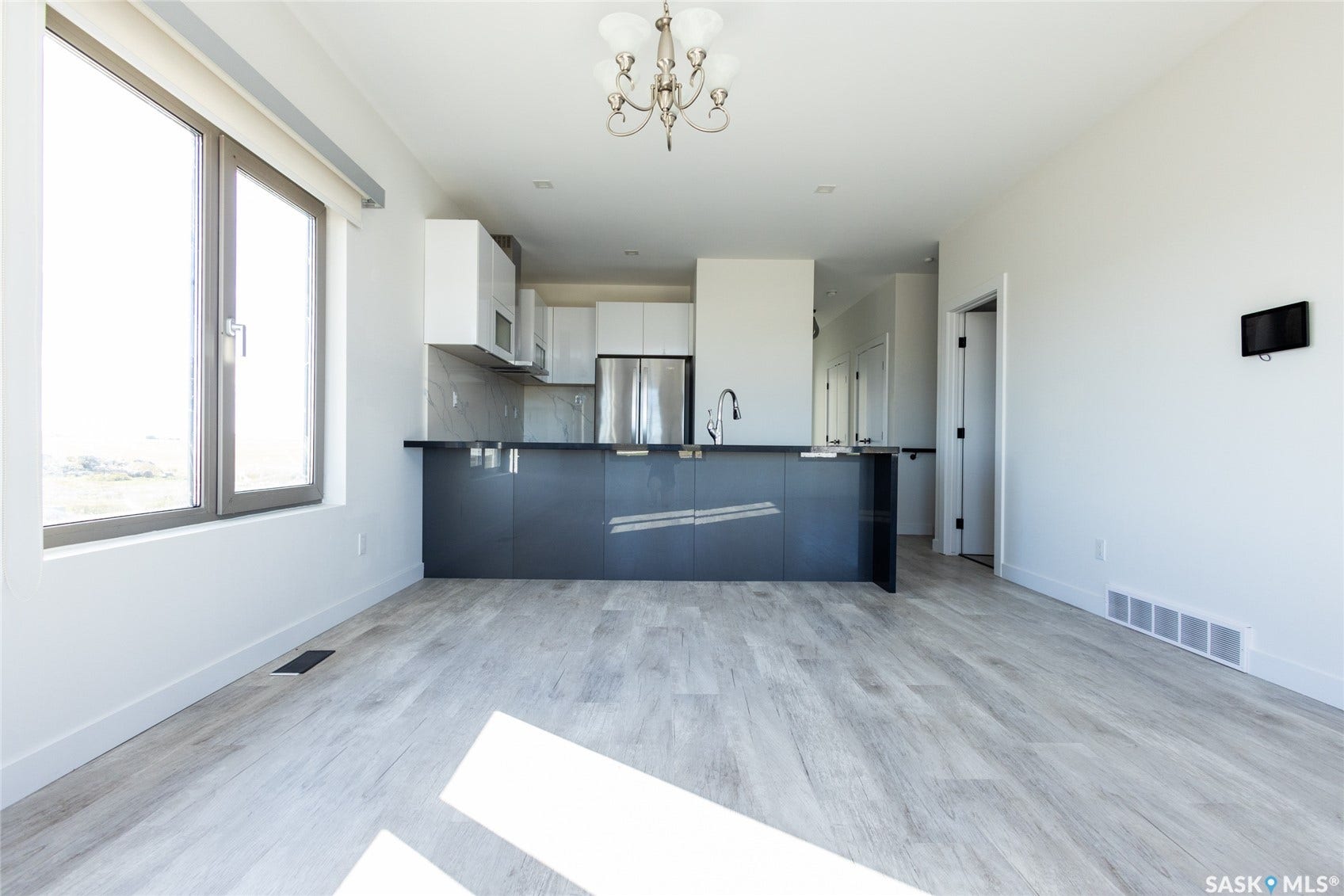 Open-concept living space with light wood-finish flooring, a contemporary kitchen island featuring a black countertop, stainless steel appliances, and a modern chandelier