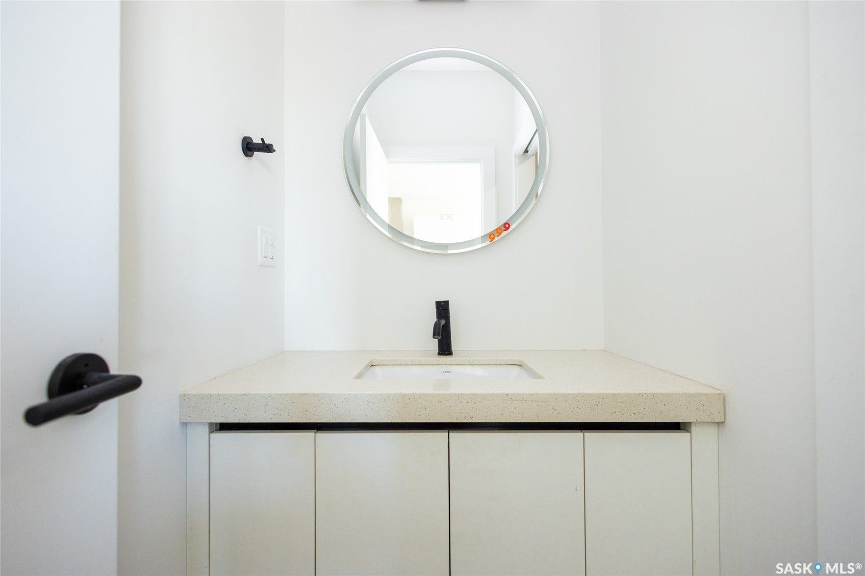 White vanity with recessed panel cabinetry, integrated sink, light-toned countertop, matte black faucet, and round mirror