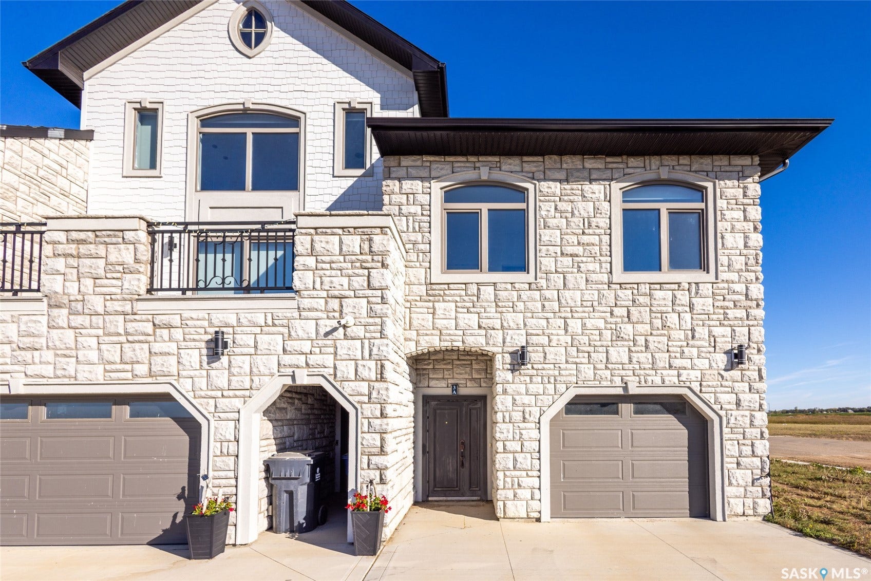 Stone veneer exterior with two integrated garage bays, an arched entry, and an upper-level balcony with black metal railings