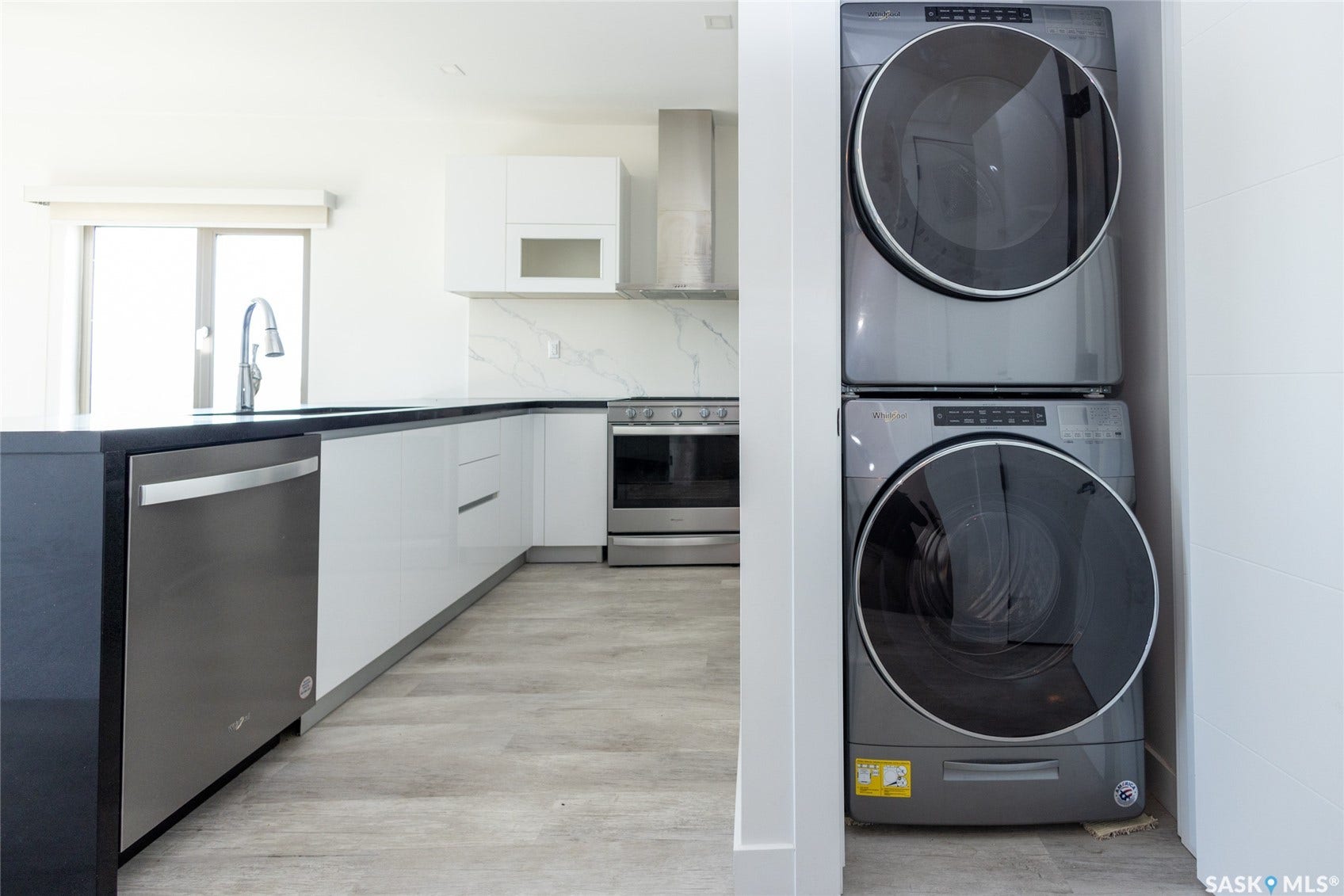 Contemporary kitchen with sleek white cabinetry, stainless steel appliances, and a stacked washer and dryer unit