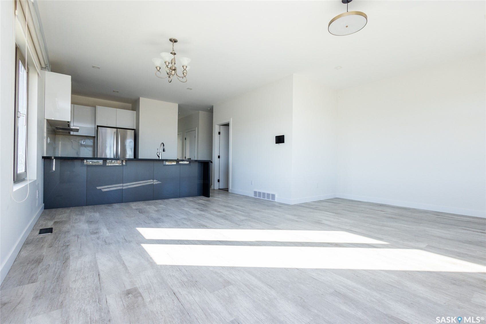 Open-concept living area with wood-finish flooring, a modern kitchen featuring white and dark cabinetry, stainless steel appliances, and a central island