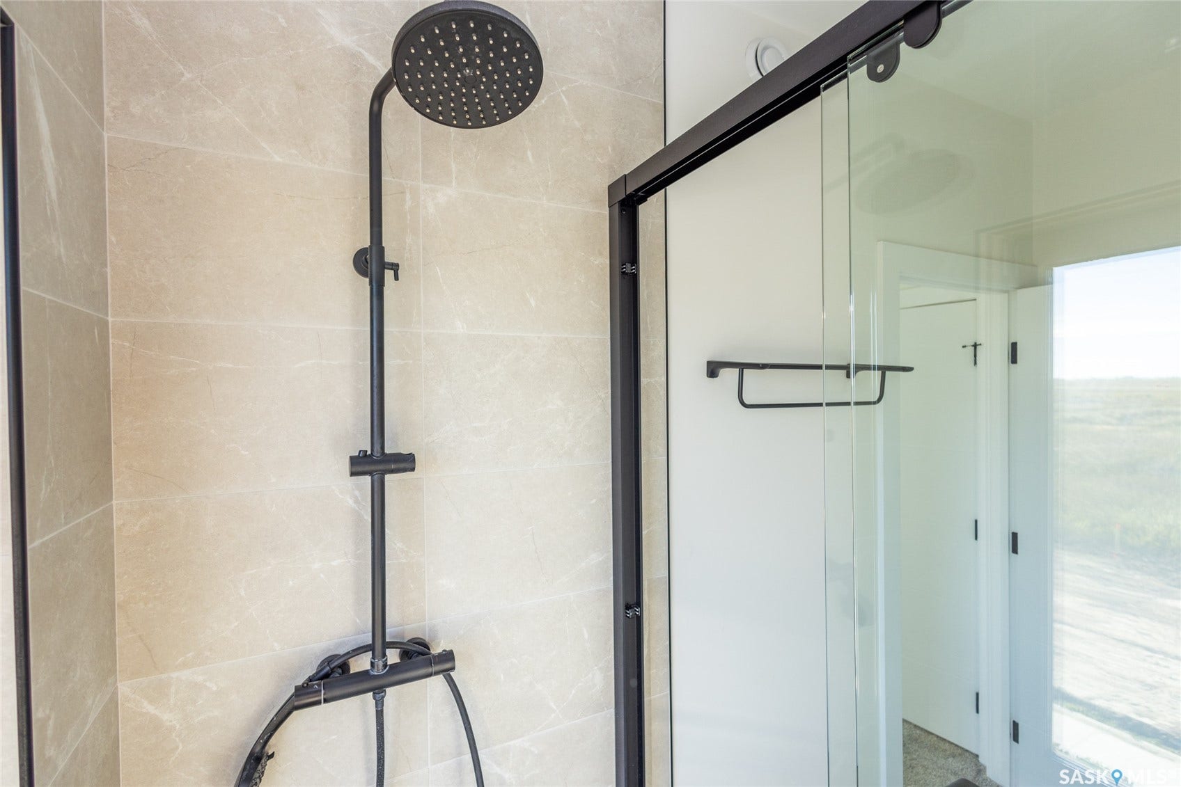 Matte black shower system with a rainfall showerhead and handheld sprayer, complemented by light-toned wall tile