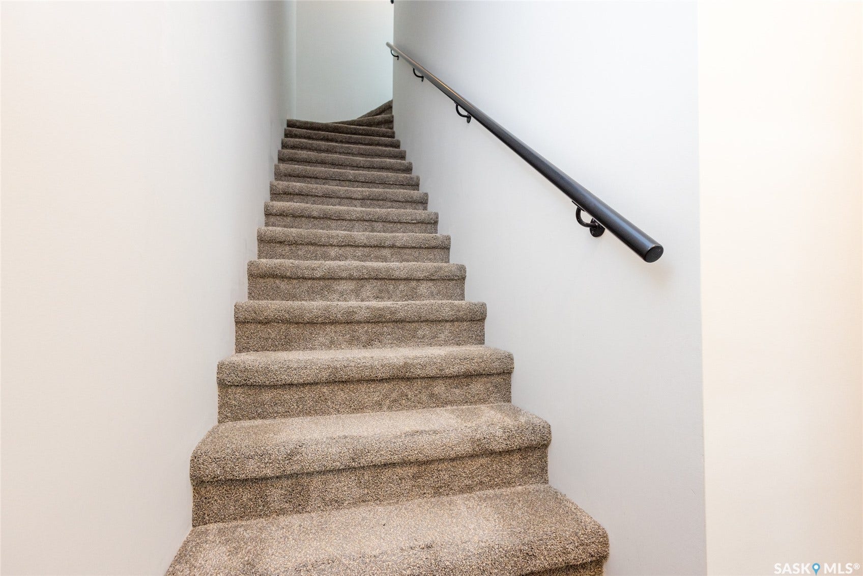 Carpeted staircase with a black handrail and neutral wall color