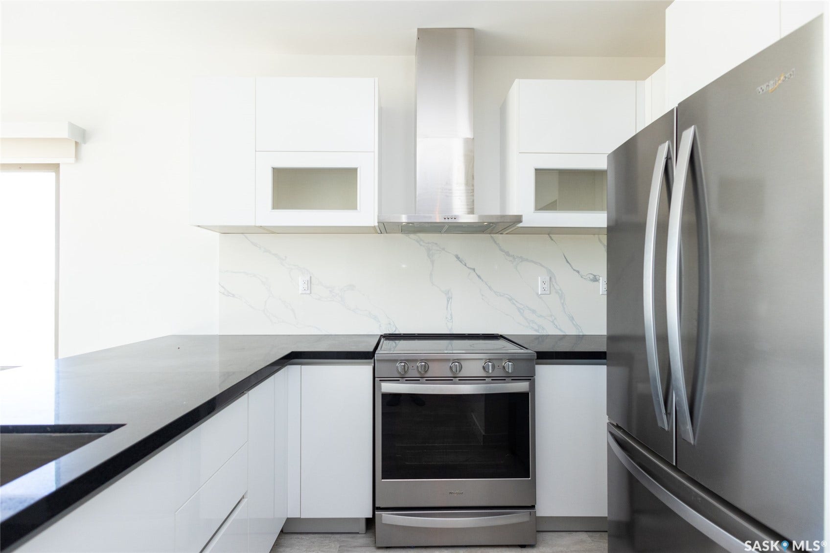 Sleek kitchen with stainless steel appliances, white cabinetry, dark countertops, and a white marble-patterned backsplash