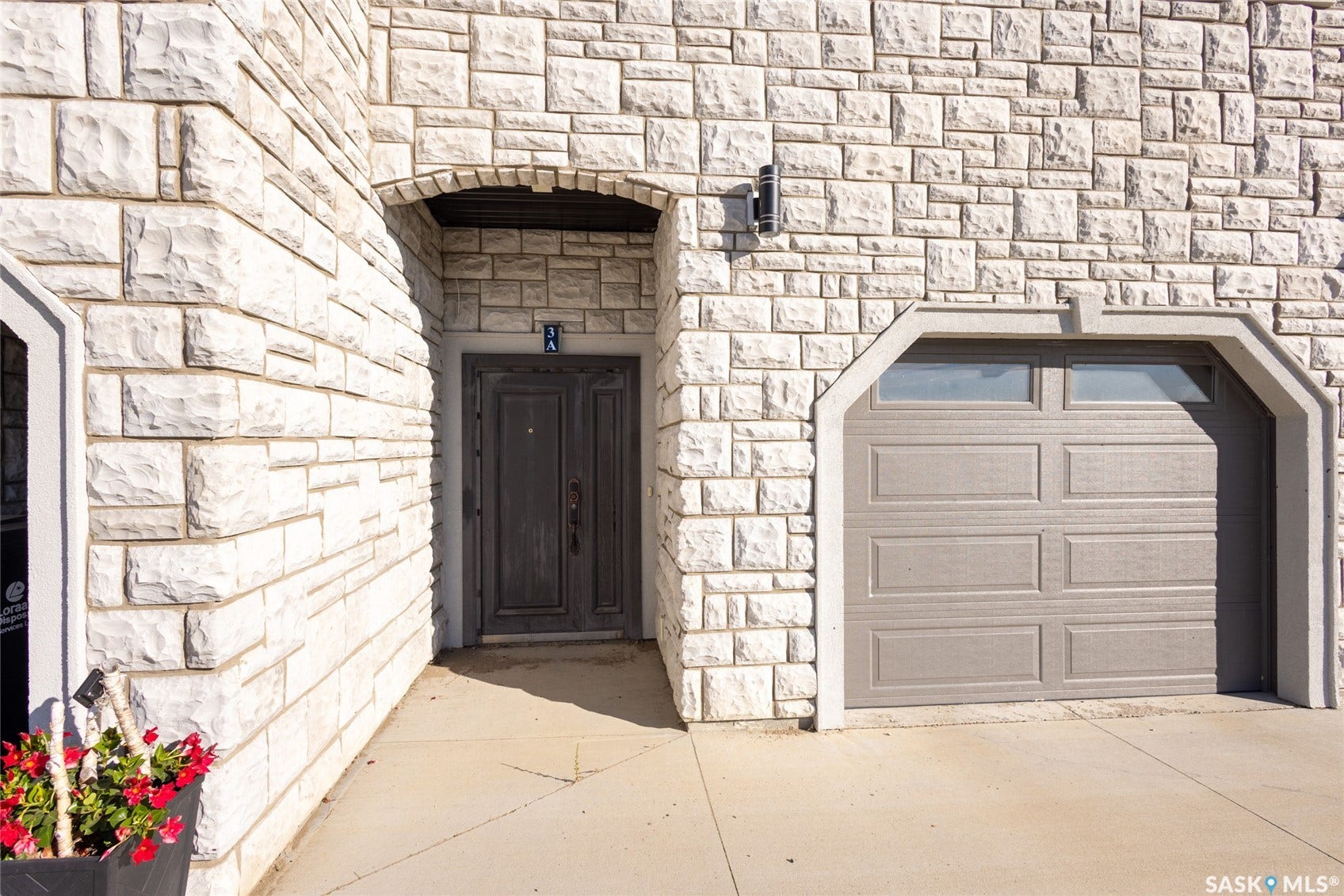 Exterior featuring white stone siding, an arched entryway with a double door, and an attached garage with an arched opening