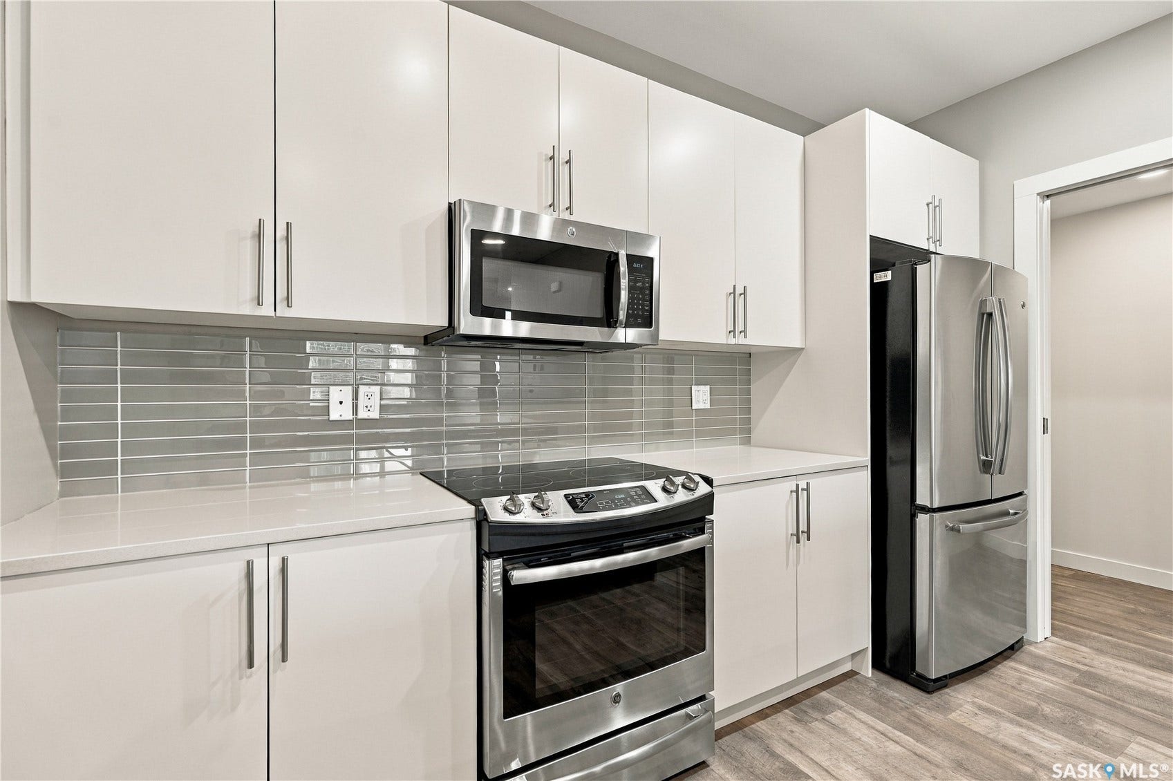 White shaker-style cabinetry with stainless steel hardware, white countertops, glass subway tile backsplash, and wood-finish flooring
