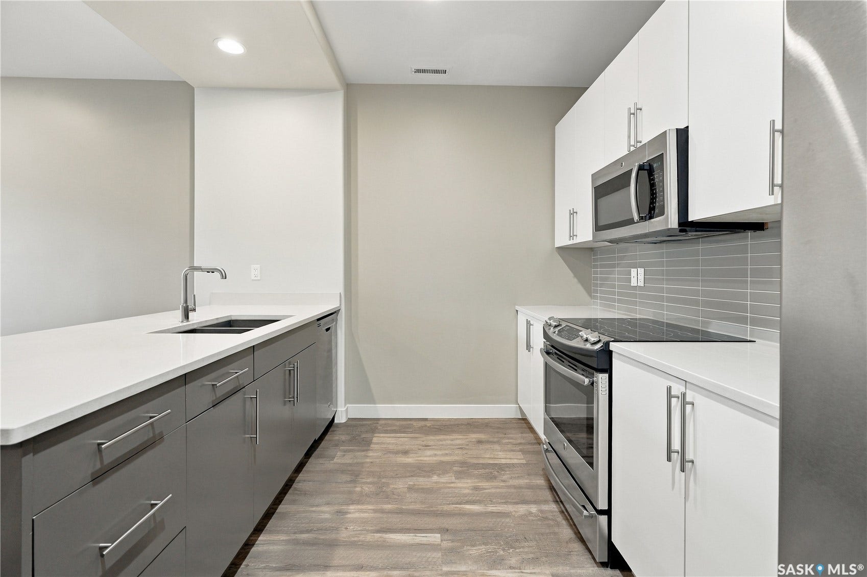 Modern kitchen with wood-finish flooring, two-tone cabinetry, stainless steel appliances, and sleek countertops