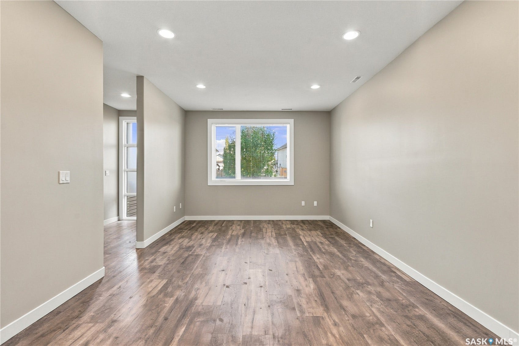 Recessed ceiling lighting, wood-finish flooring, white trim, and a window providing natural illumination