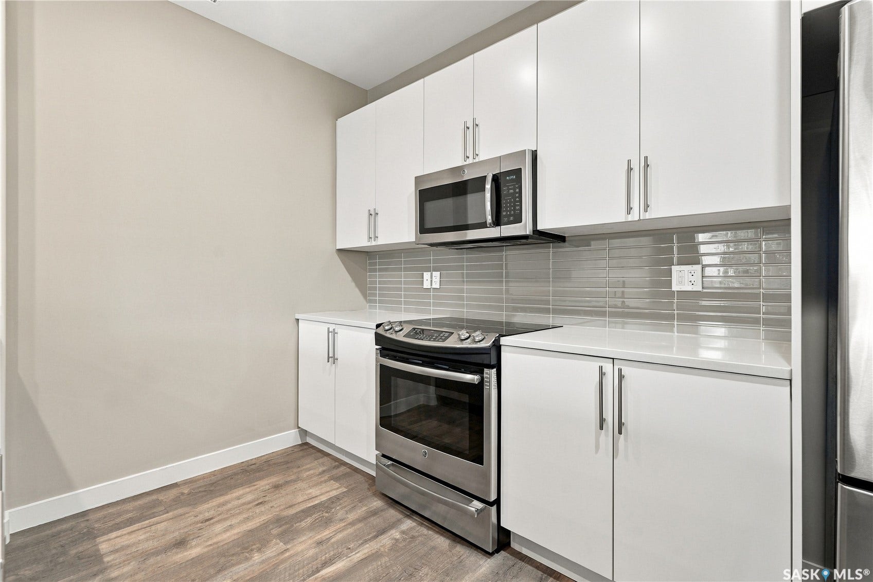 White cabinetry, stainless steel appliances, light-colored countertops, tile backsplash, and wood-finish flooring