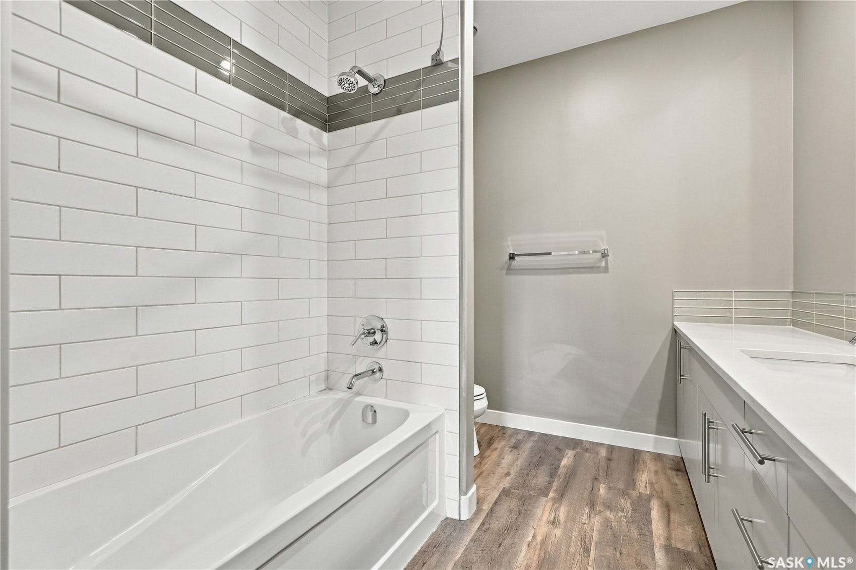 Bathtub and shower combination featuring subway tile surround with accent band, chrome fixtures, wood-finish flooring, and a vanity with an integrated sink and backsplash