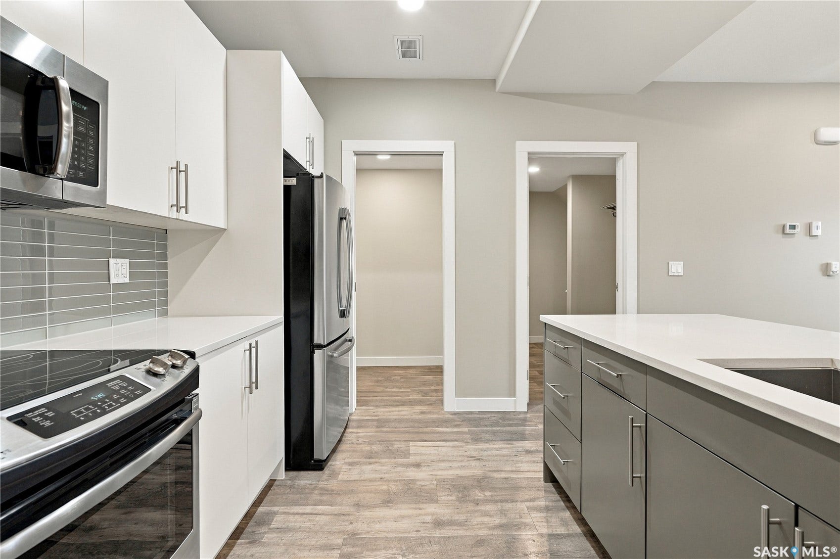 Modern kitchen featuring stainless steel appliances, white cabinetry, a tiled backsplash, and wood-finish flooring