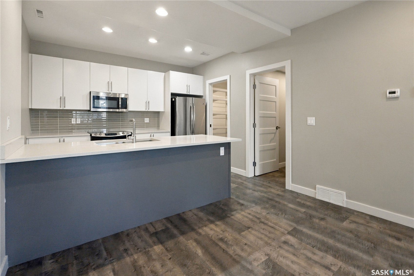 Open-concept kitchen featuring an expansive island with white countertop, white upper cabinetry, stainless steel appliances, and wood-finish flooring