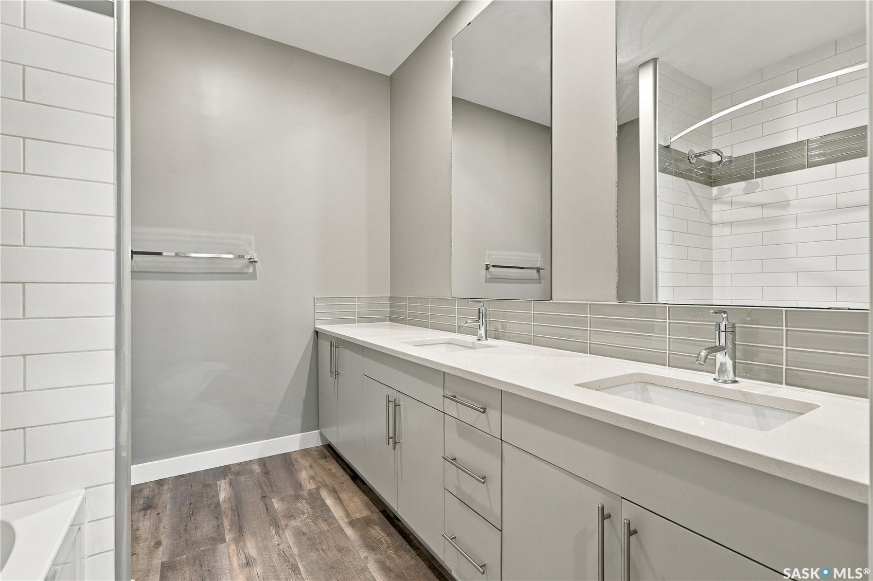 Dual vanity with integrated sinks, light-toned countertops, wood-finish flooring, full-width mirrors, and subway tile shower surround