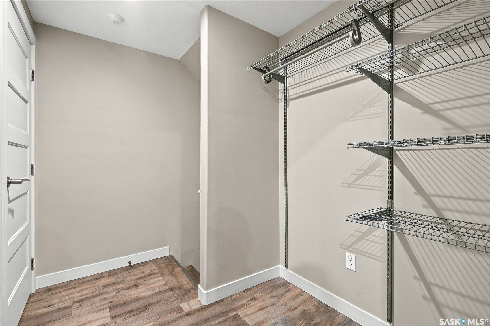 Wood-finish flooring, white trim, a modern door with a lever handle, and wire shelving system