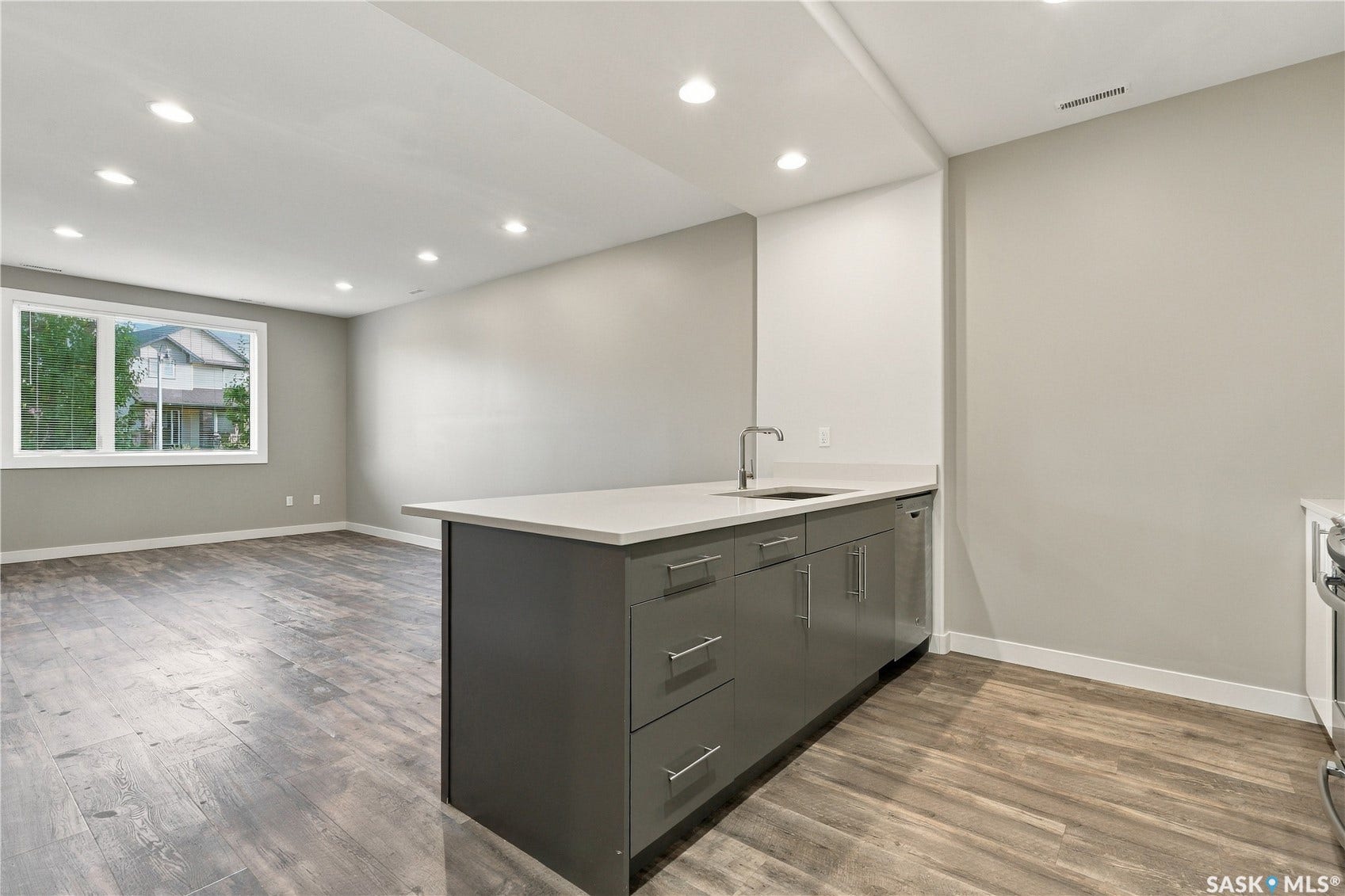 Expansive open-concept space featuring wood-finish flooring, a kitchen island with sink and stainless steel dishwasher, a large window, and recessed lighting