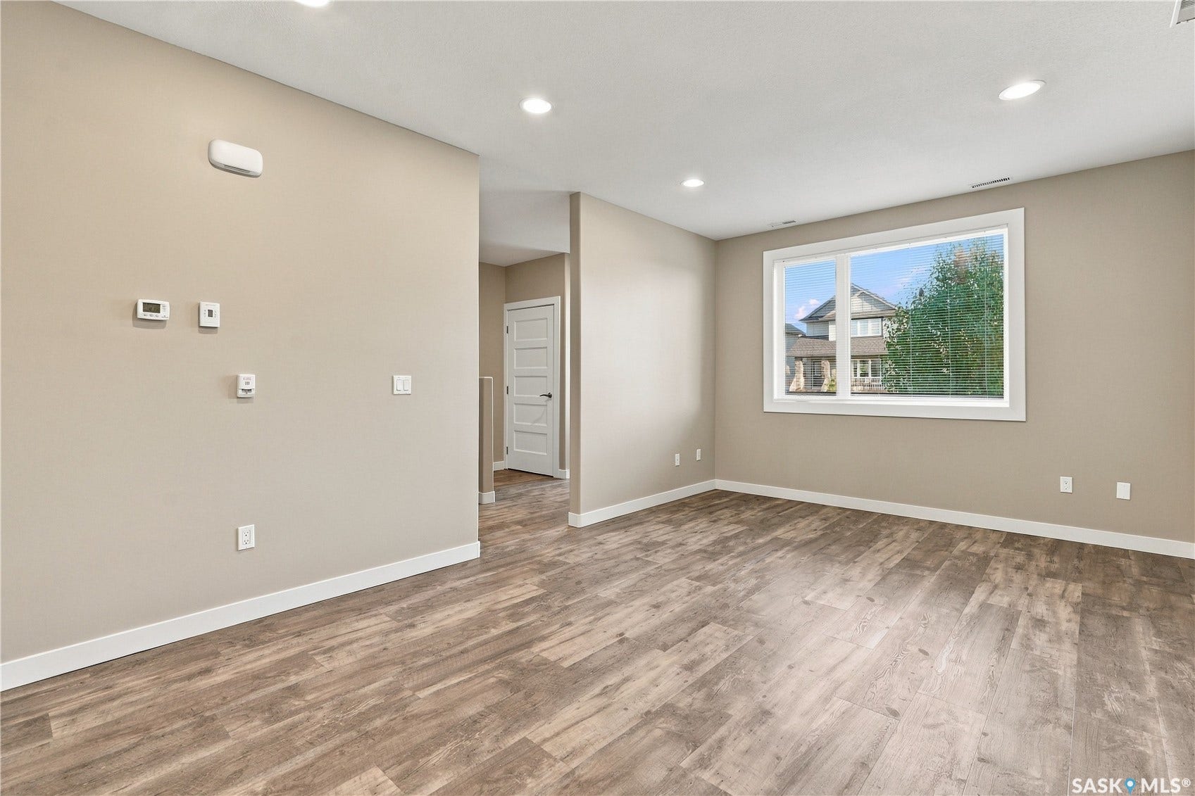 Recessed lighting, wood-finish flooring, neutral paint palette, white trim, and a large window