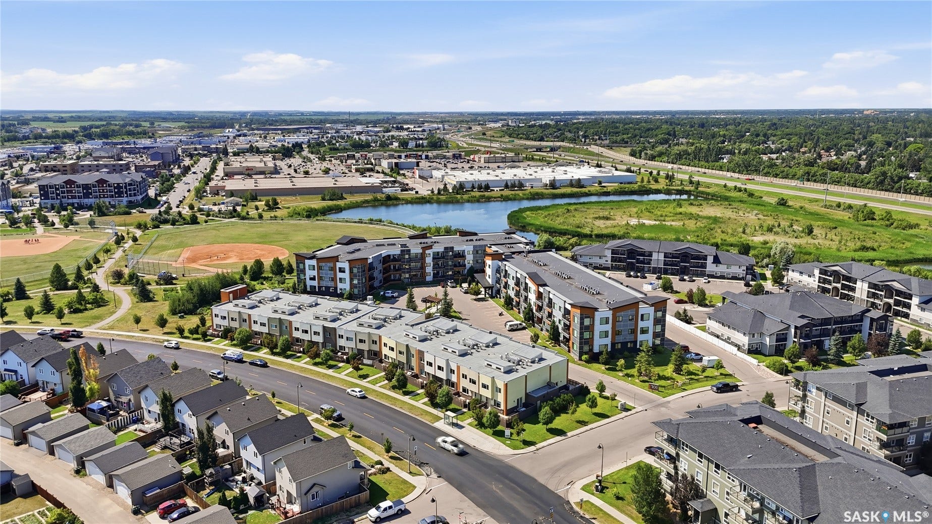 Aerial perspective showcasing a residential community with varied architectural styles, a prominent baseball diamond, and a natural pond feature