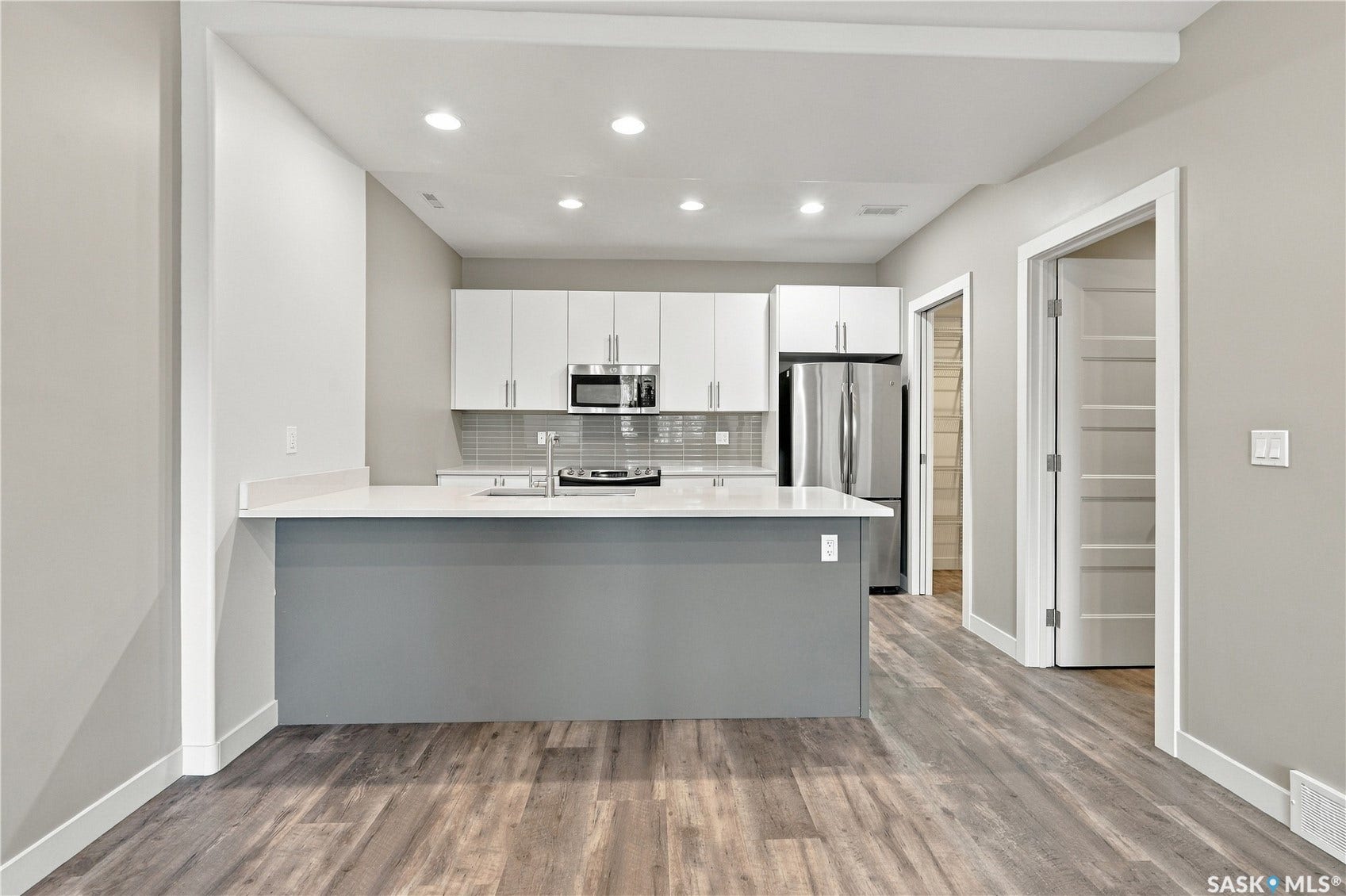 Modern kitchen featuring white cabinetry, stainless steel appliances, a center island with countertop seating, and wood-finish flooring