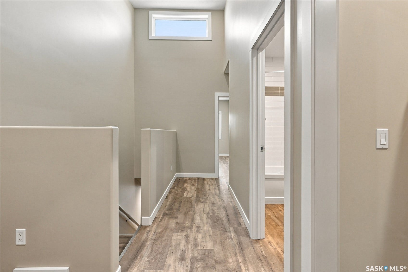 Hallway with wood-finish flooring, light neutral paint, white trim, and a high transom window