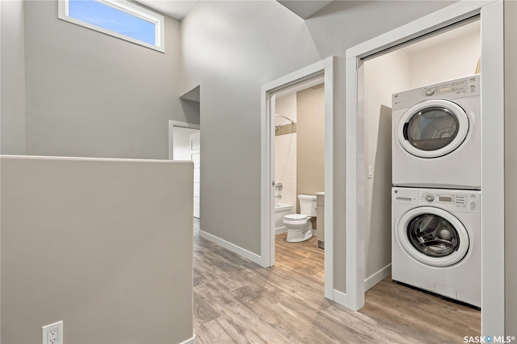 Recessed laundry area with stacked appliances, wood-finish flooring, and a transom window
