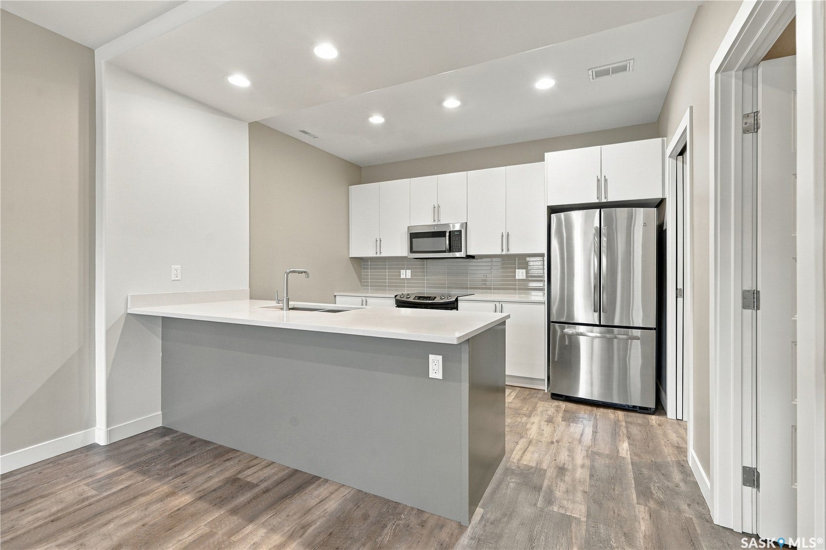 Modern kitchen featuring a large island, stainless steel appliances, white cabinetry, and wood-finish flooring