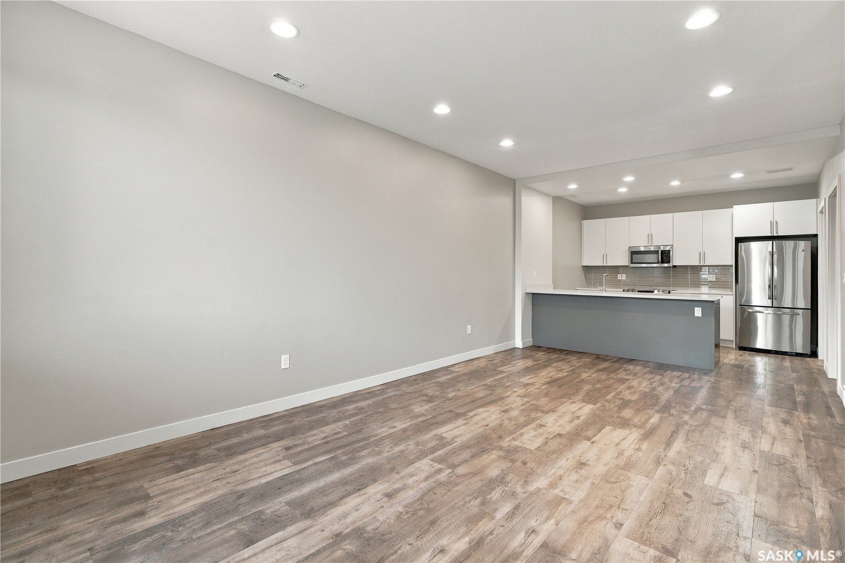 Open concept kitchen with a central island, stainless steel refrigerator, microwave, and wood-finish flooring