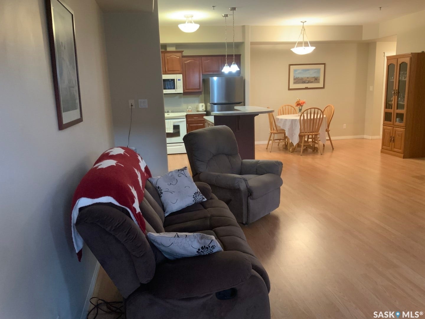 Open-concept living area featuring wood-finish flooring, a kitchen with wood cabinetry and stainless steel appliances, and a dining area with a pendant light fixture