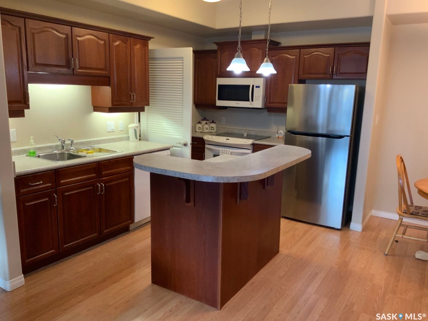 Full kitchen featuring wood-finish cabinetry, light-toned countertops, stainless steel refrigerator, microwave, and wood-finish flooring